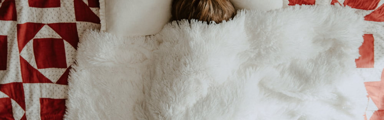 Frau im Bett mit der Decke über dem Kopf